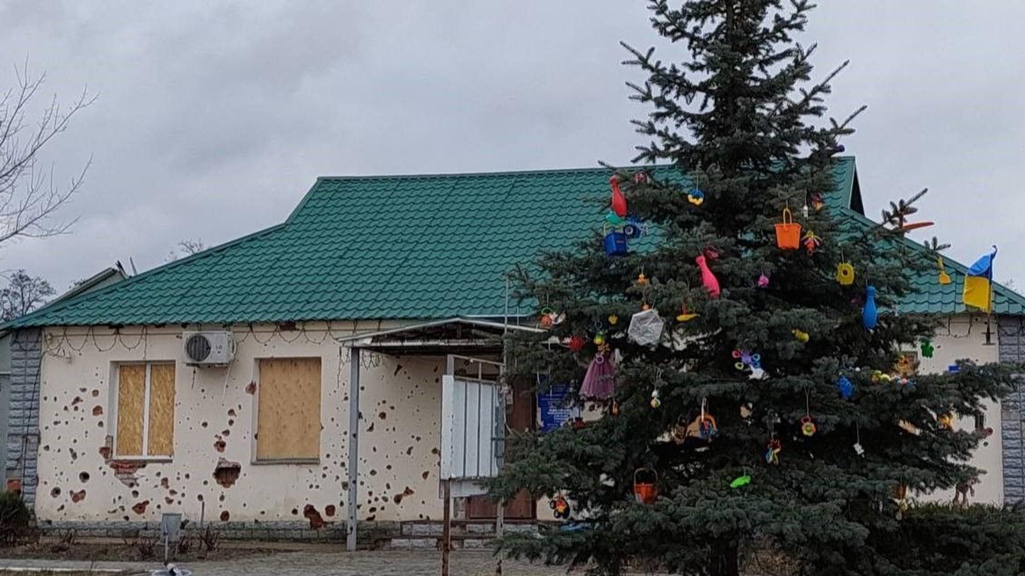 Ein mit Kinderspielzeug geschmückter Baum steht vor einem kaputten Haus.