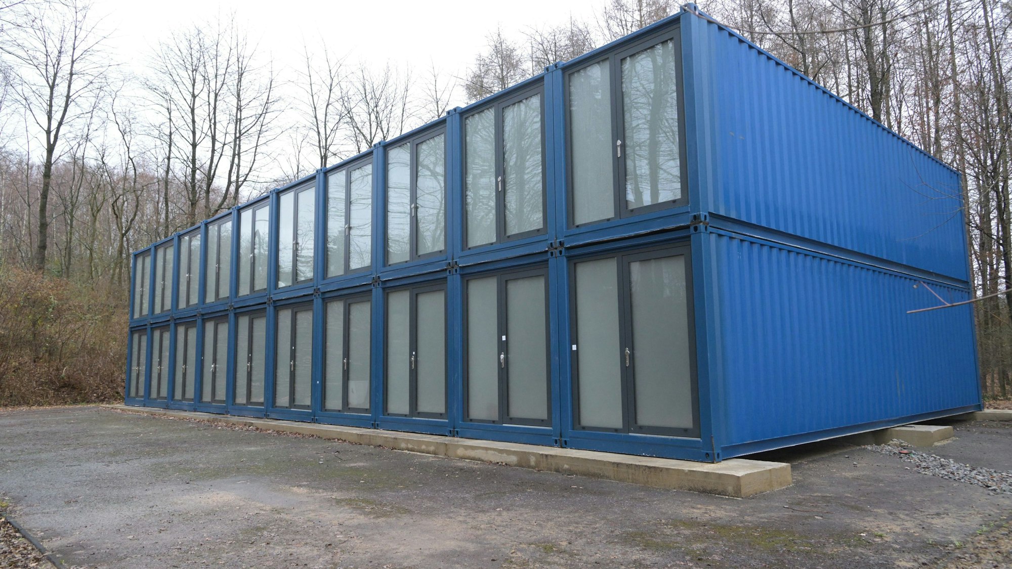 Blaue Container stehen auf einem Platz am Wald.