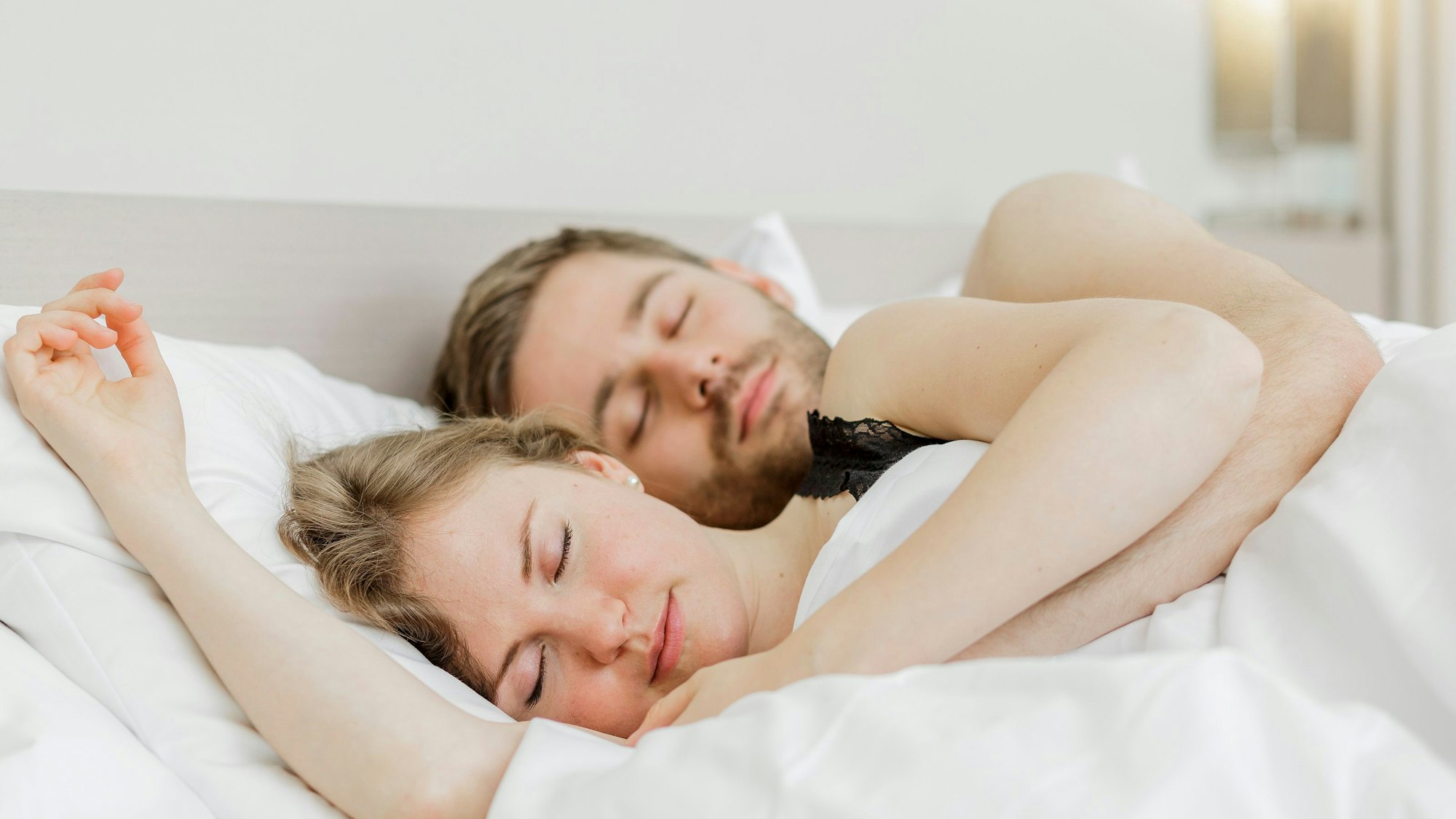 Eine Frau und ein Mann liegen aneinandergekuschelt im Bett und schlafen.