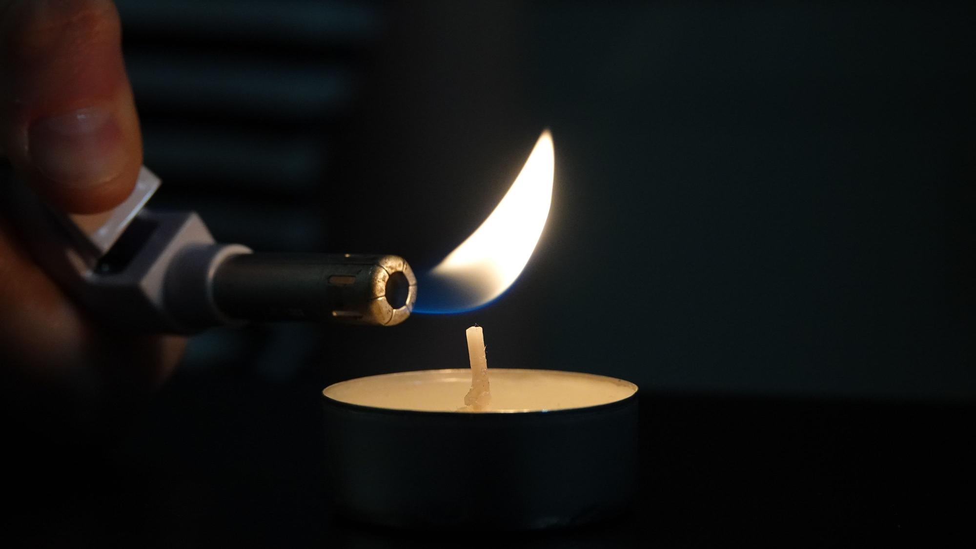 Eine Frau zündet mit einem Feuerzeug ein Teelicht an.