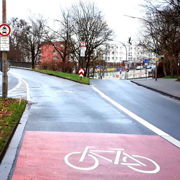 Eine Straße verzweigt sich, im Vordergrund ist ein großes Rad-Piktogramm zu sehen.