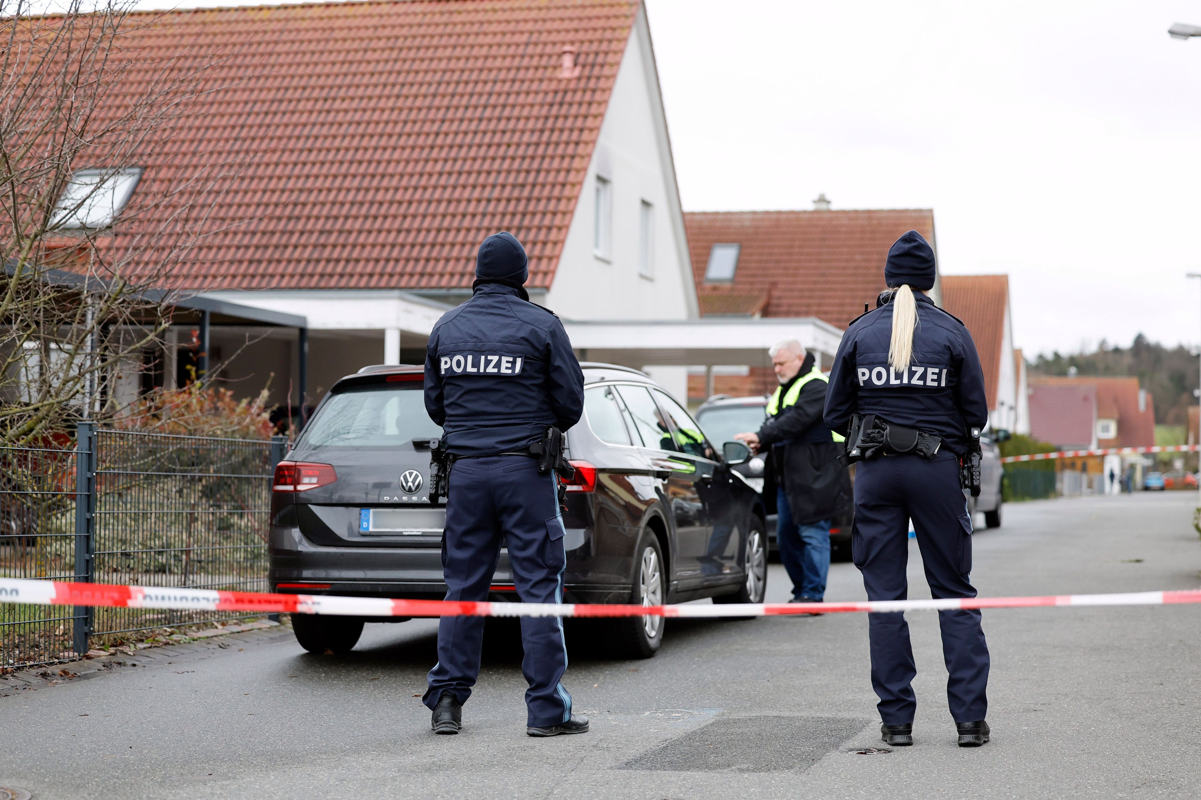 Polizeibeamte stehen in der Nähe des Wohnhauses, in dem es zu einer Gewalttat gekommen sein soll, man sieht sie von hinten.