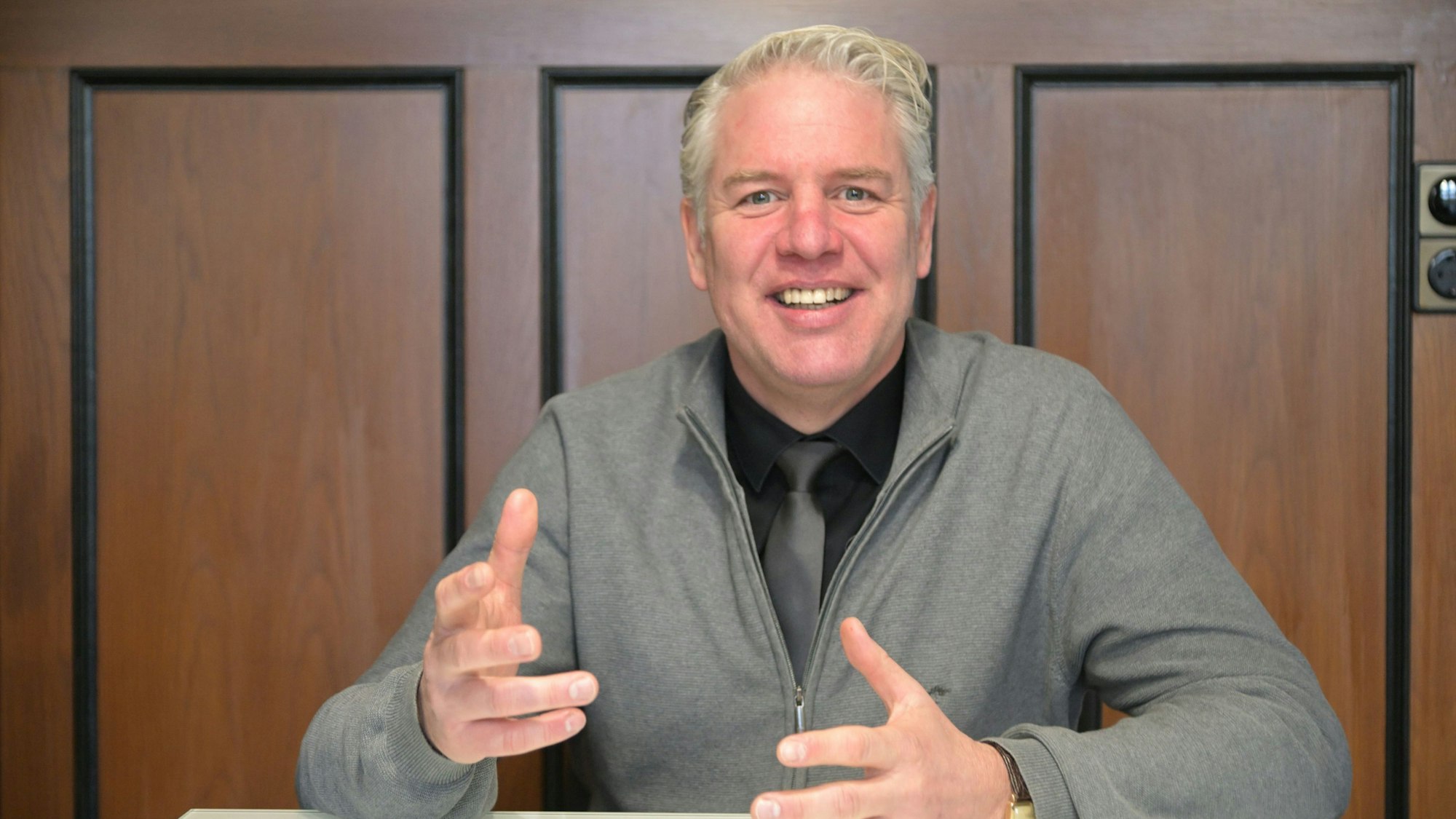 Robert Lennerts, Bürgermeister von Odenthal, sitzt vor einer Holzwand an einem Tisch und gestikuliert.