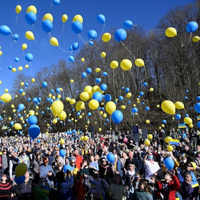 Hunderte Menschen lassen gelbe und blaue Luftballons in die Luft steigen.