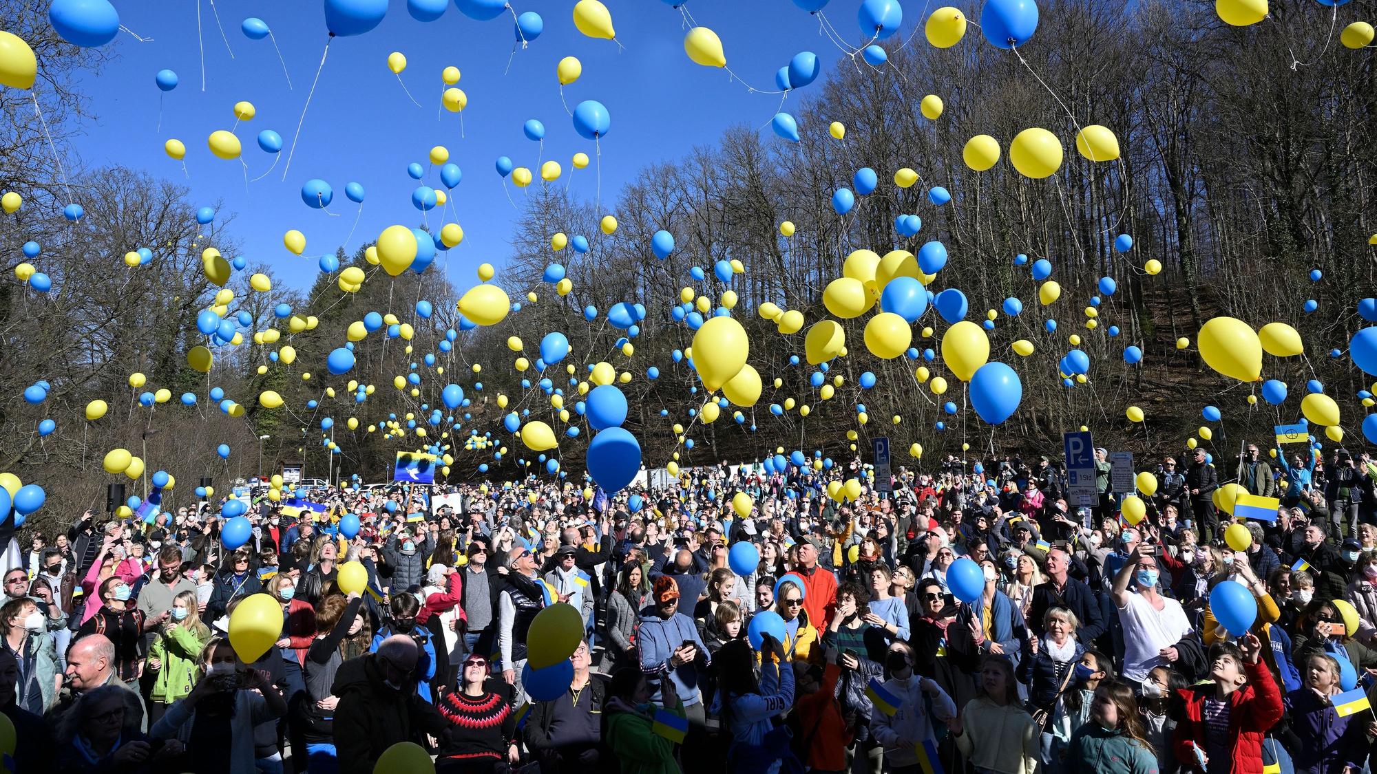 Hunderte Menschen lassen gelbe und blaue Luftballons in die Luft steigen.