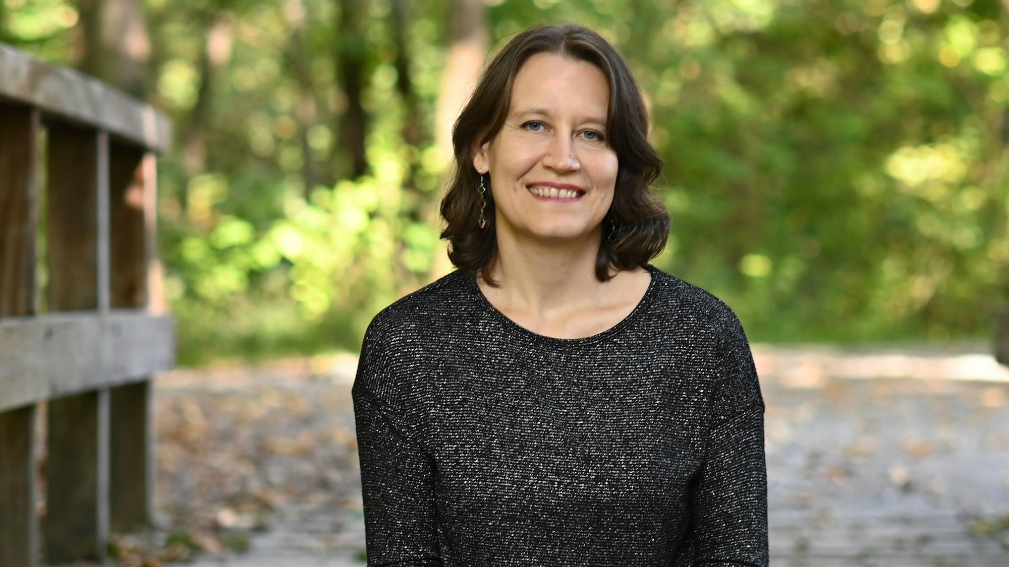 Elvira Zeißler sitzt mit einigen ihrer Bücher auf dem Schoß auf einem Holzsteeg.