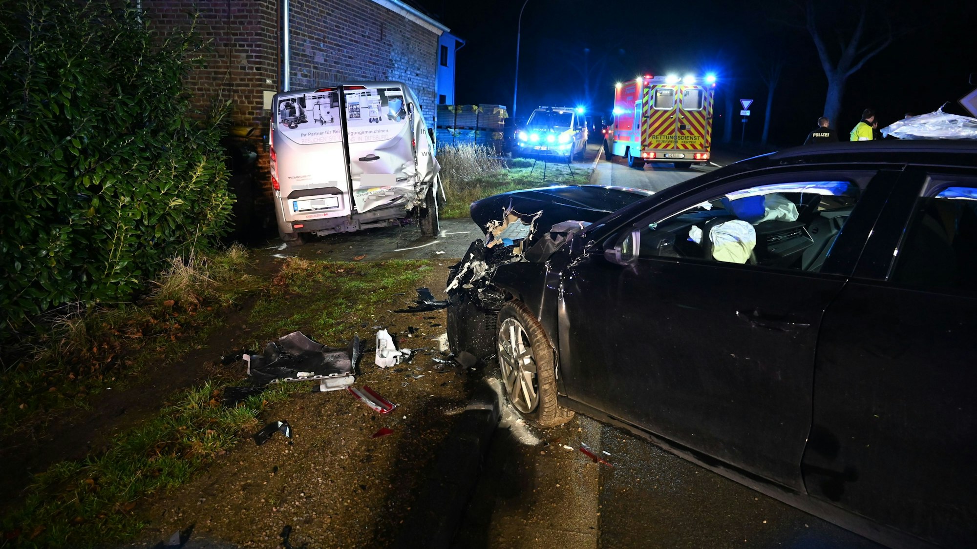 Unfallstelle in Kerpen. Zu sehen sind beide involvierten Fahrzeuge, ein schwarzer Audi hat einen frotalen Schaden, ein silberner Transporter ist hinten rechts beschädigt. Im Hintergrund Polizei- und Rettungswagen mit Blaulicht.