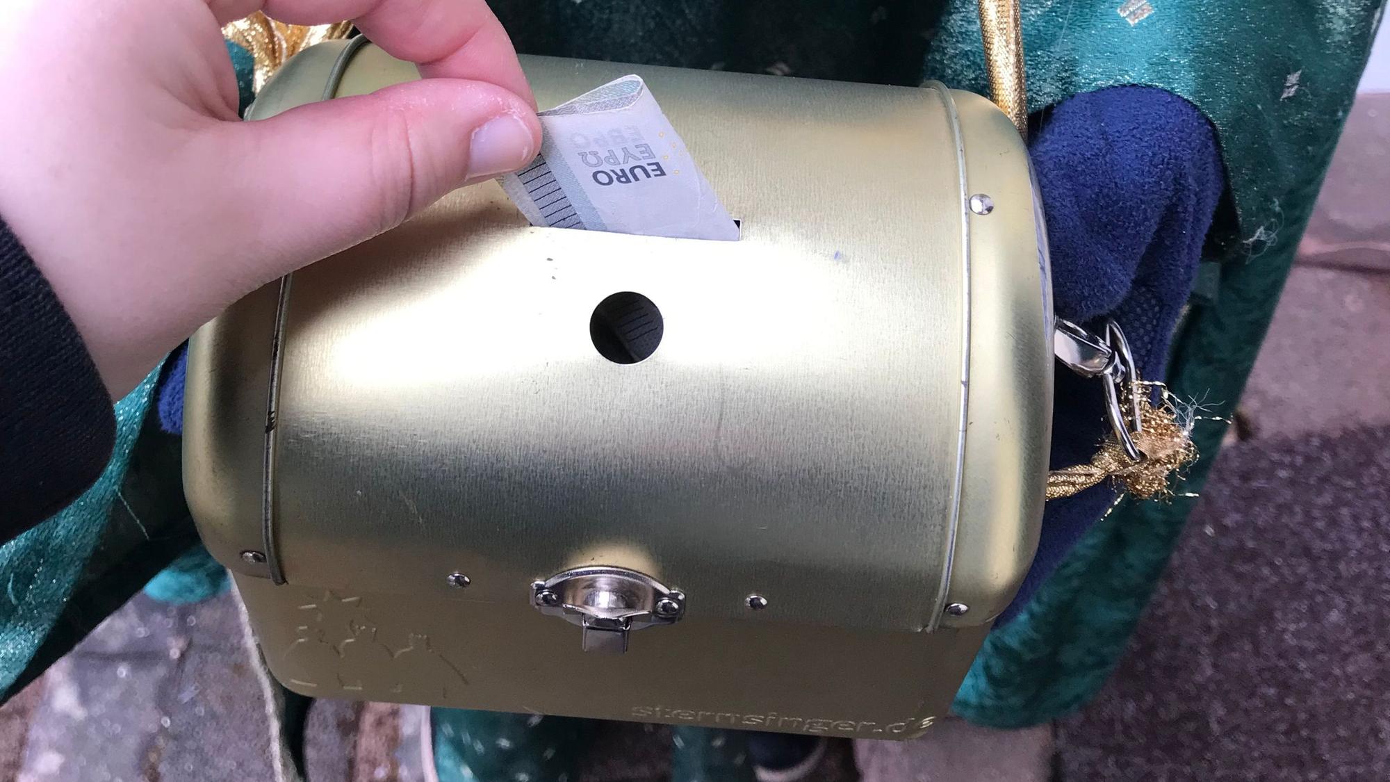 Ein Geldschein wird in die Spendendose eingeworfen.