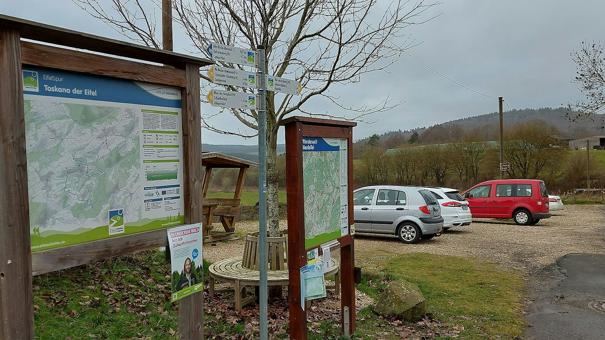 Einige Autos sind auf einem Wanderparkplatz hinter Hinweisschildern geparkt.
