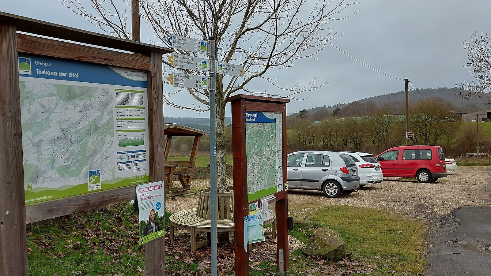 Einige Autos sind auf einem Wanderparkplatz hinter Hinweisschildern geparkt.