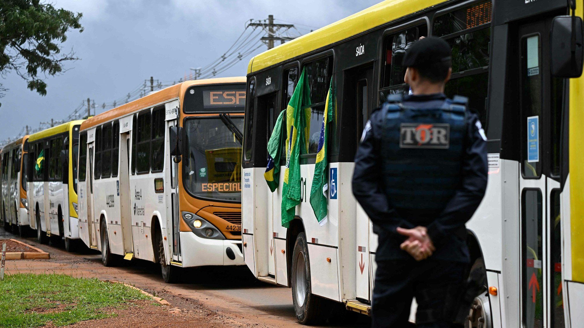 Mehrere Busse mit Anhängern des ehemaligen brasilianischen Präsidenten Jair Bolsonaro fahren in Richtung eines Gefängnisses. Die Polizei beobachtet den Transport.