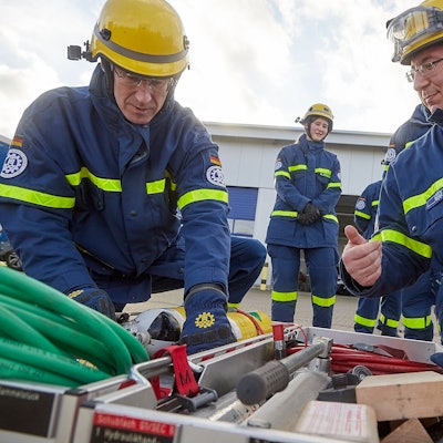 Zwei Männer mit THW-Uniformen hocken vor einer Kiste mit Werkzeugen.