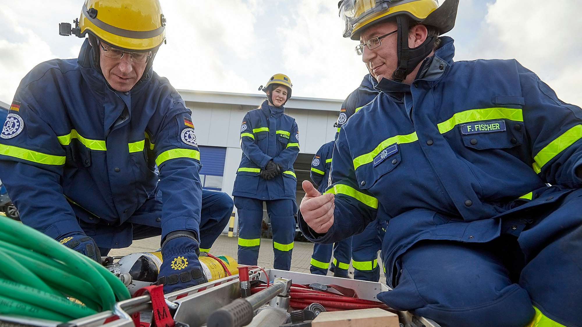 Zwei Männer mit THW-Uniformen hocken vor einer Kiste mit Werkzeugen.