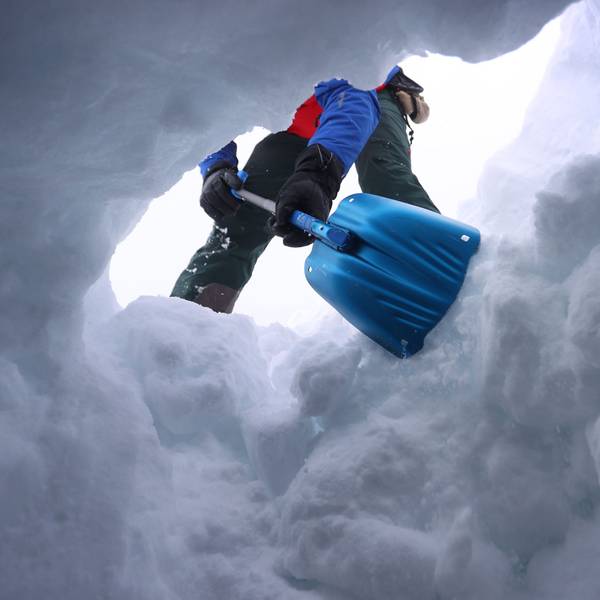 Ein Mensch schaufelt den Eingang zu einem Schneeloch frei