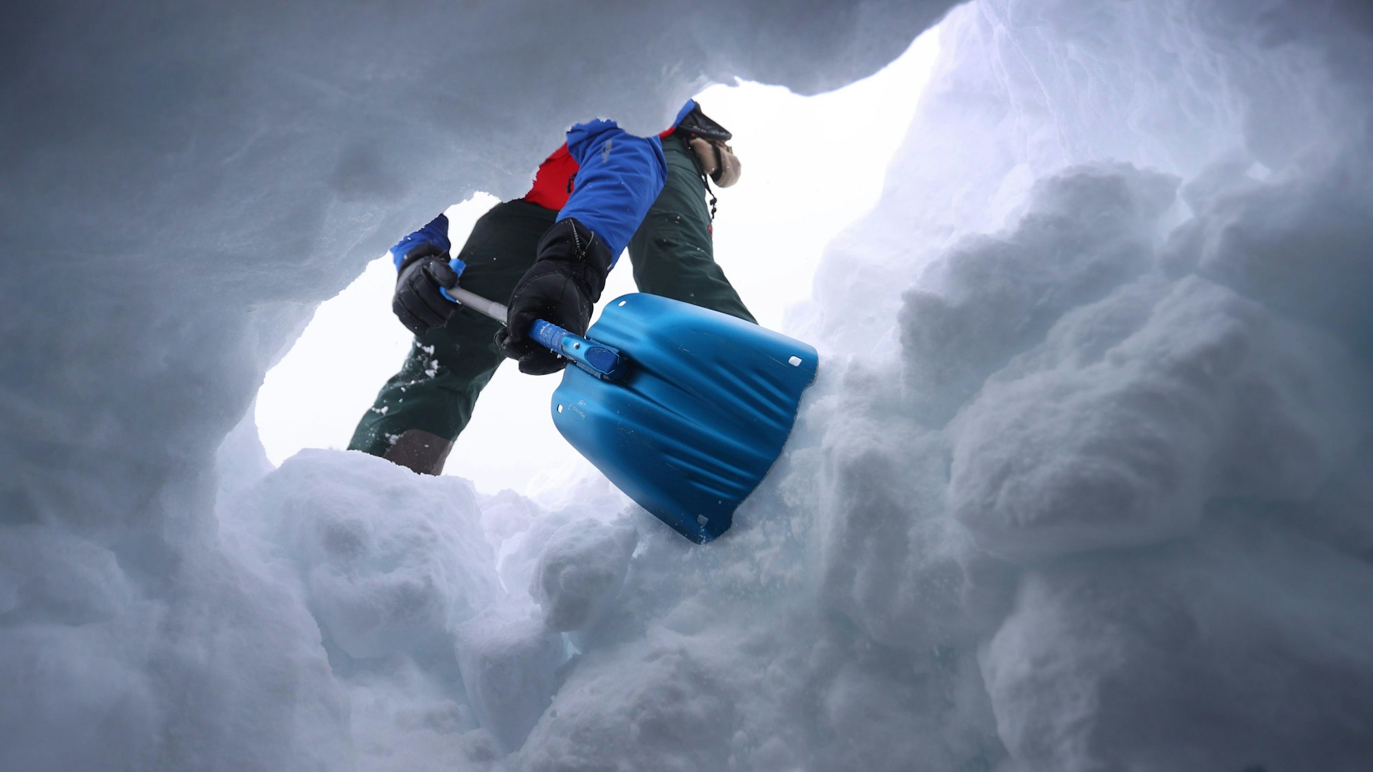 Ein Mensch schaufelt den Eingang zu einem Schneeloch frei