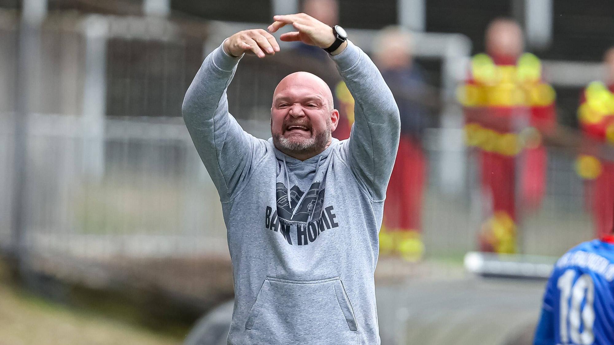 Ein Mann in einem grauen Kapuzenpullover gestikuliert mit den Armen.