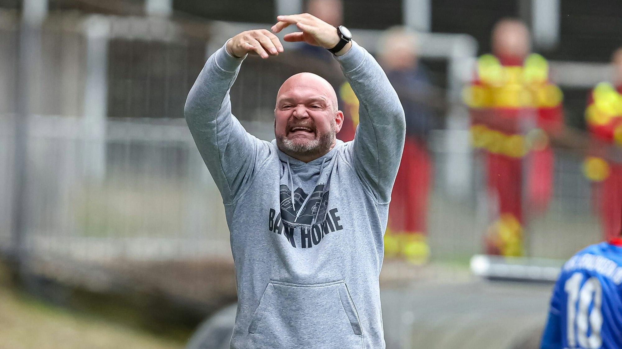 Ein Mann in einem grauen Kapuzenpullover gestikuliert mit den Armen.