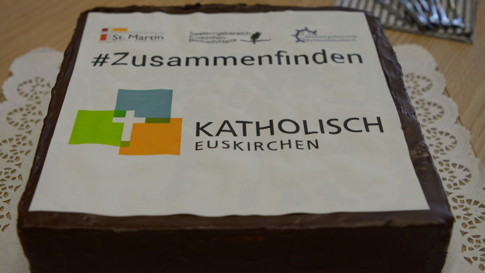 Pfarrer Tobias Hopmann schneidet den Kuchen an, der das Logo der neuen pastoralen Einheit Euskirchen zeigt.