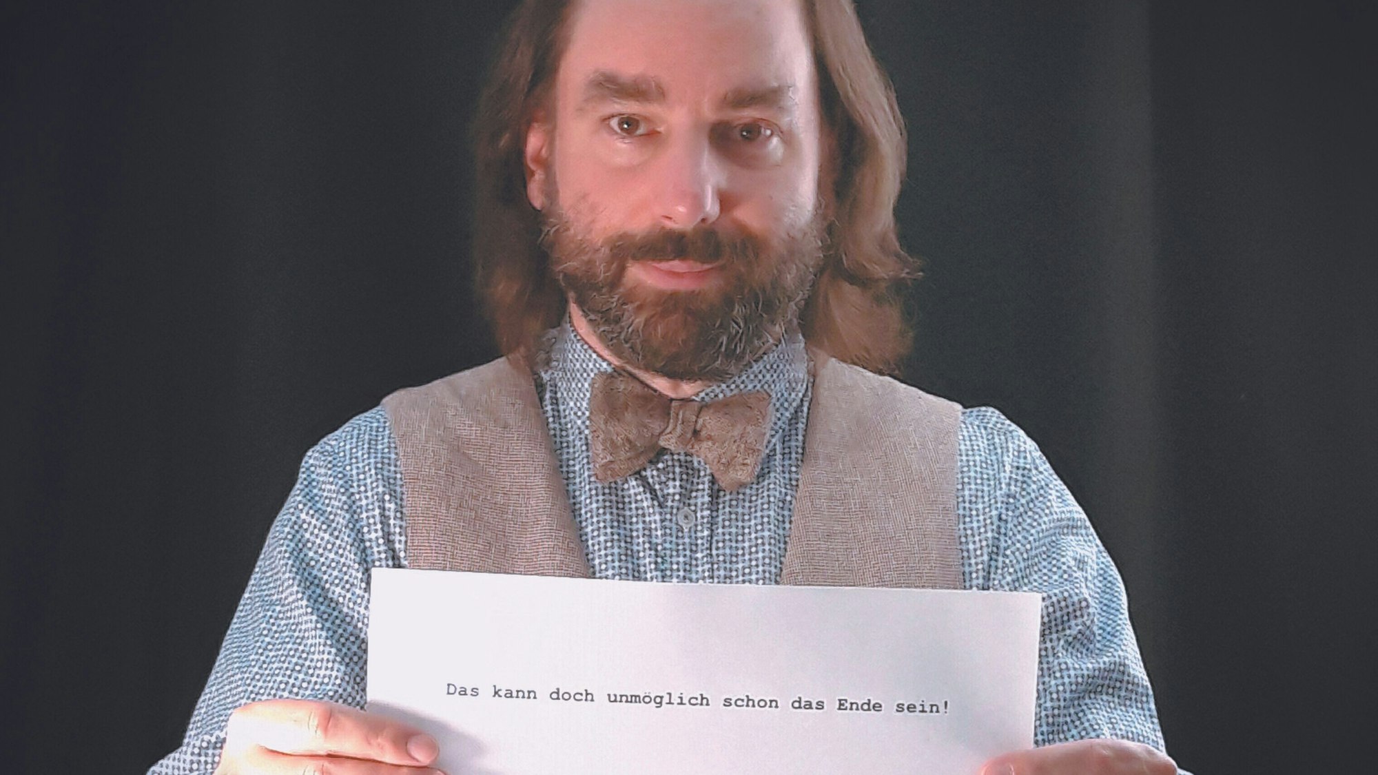 Autor Alexander Bach halt einen Zettel mit dem Satz „Das kann doch unmöglich schon das Ende sein“ in die Kamera.