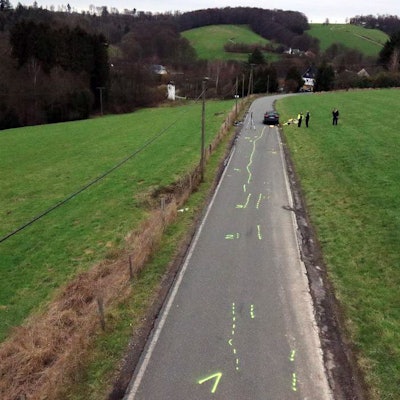 Ein Unfallaufnahmeteam der Polizei sichert Spuren auf einer Kreisstraße, auf der Kreidemarkierungen zu sehen sind.