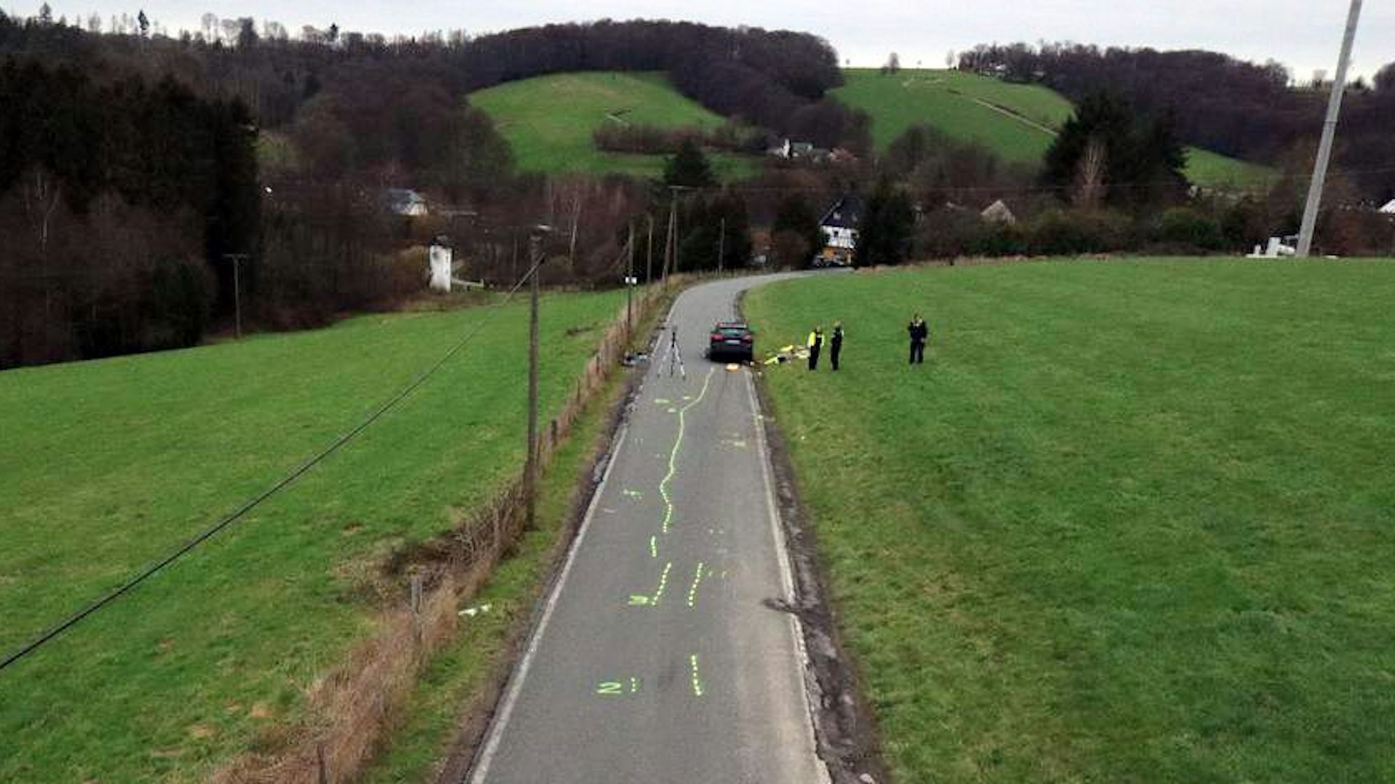 Auf einer Straße sind gelbe Markierungen zu sehen. Polizisten nehmen die Spuren eines Unfalls auf.