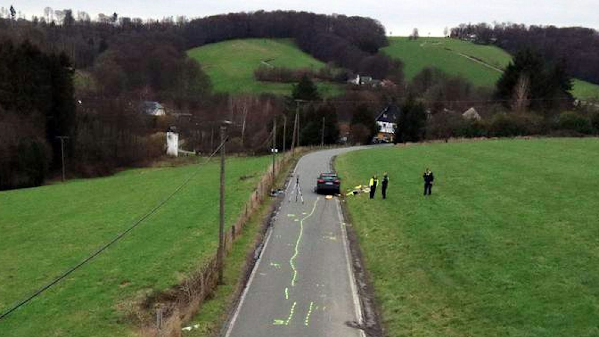 Auf einer Straße sind Unfallmarkierungen zu sehen. Polizisten sichern Spuren.