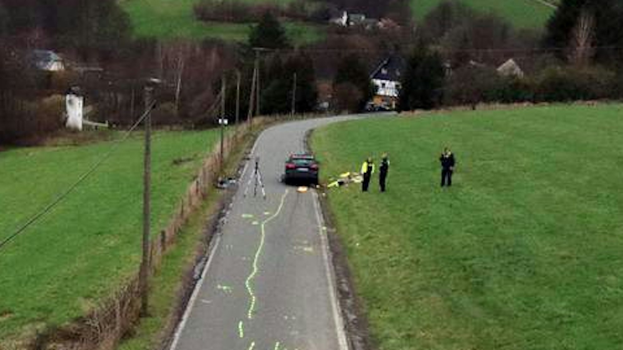 Ein Unfallaufnahmeteam der Polizei sichert Spuren auf einer Kreisstraße, auf der Kreidemarkierungen zu sehen sind.