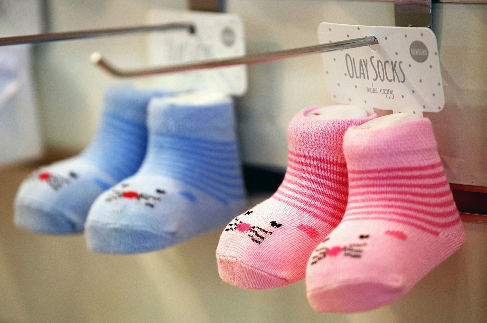 Hellblaue und rosafarbene Babysöckchen hängen in einem Regal.