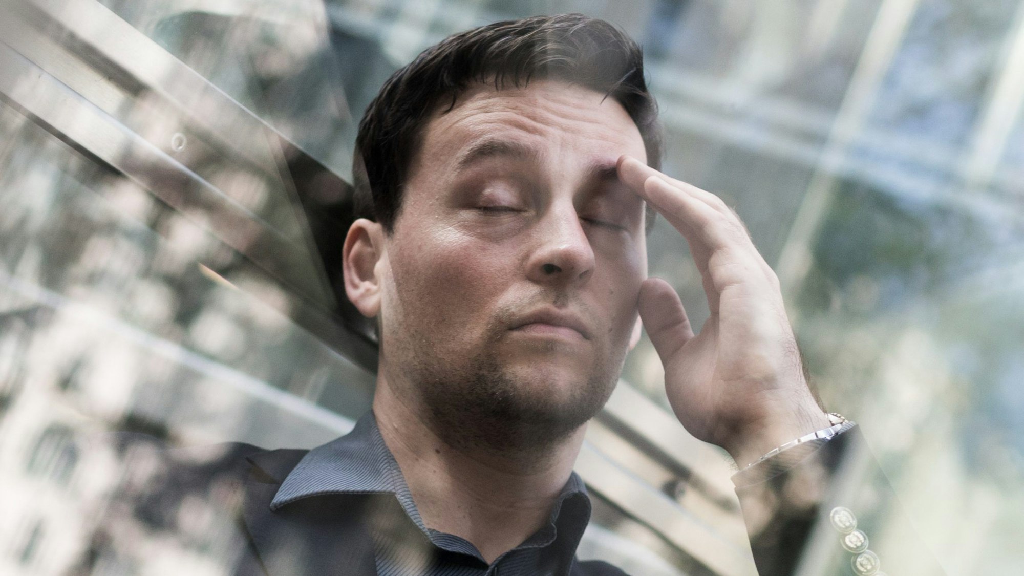 Ein Mann leidet unter Stress: Er hat die Augen geschlossen und fasst sich an den Kopf.