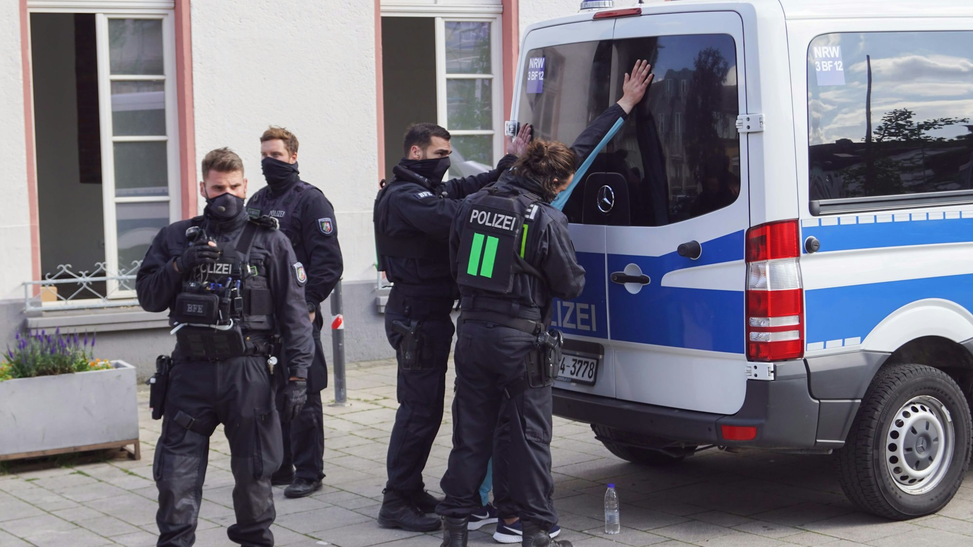 Polizisten stehen vor einem Einsatzwagen und haben eine Person in Gewahrsam genommen.