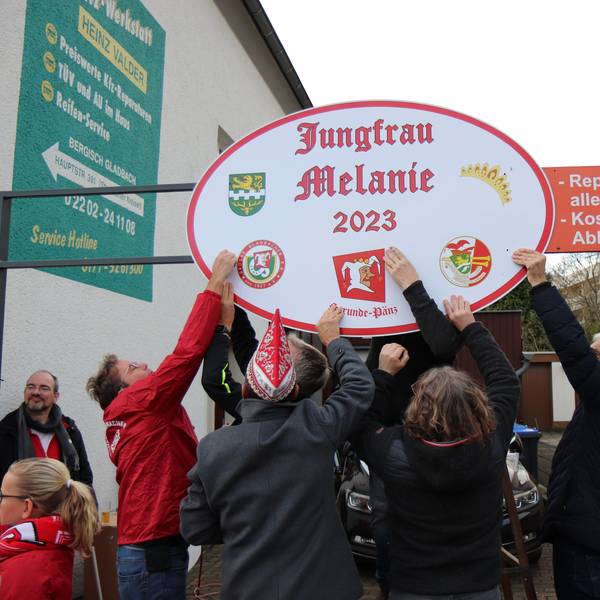 Karnevalisten bringen ein Schild mit der Aufschrift „Jungfrau Melanie 2023“ an.