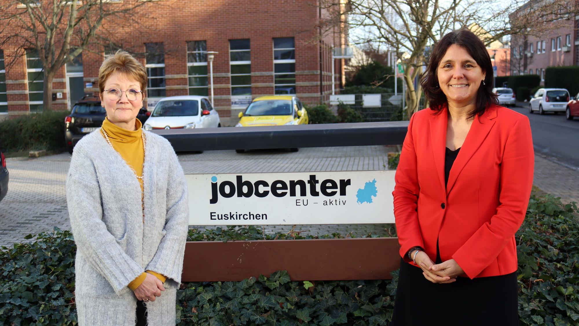 Astrid Hahn (l.) vom Jobcenter Eu-aktiv und Anja Daub von der Agentur für Arbeit Brühl stehen vor dem Schild des Jobcenters Eu-aktiv.
