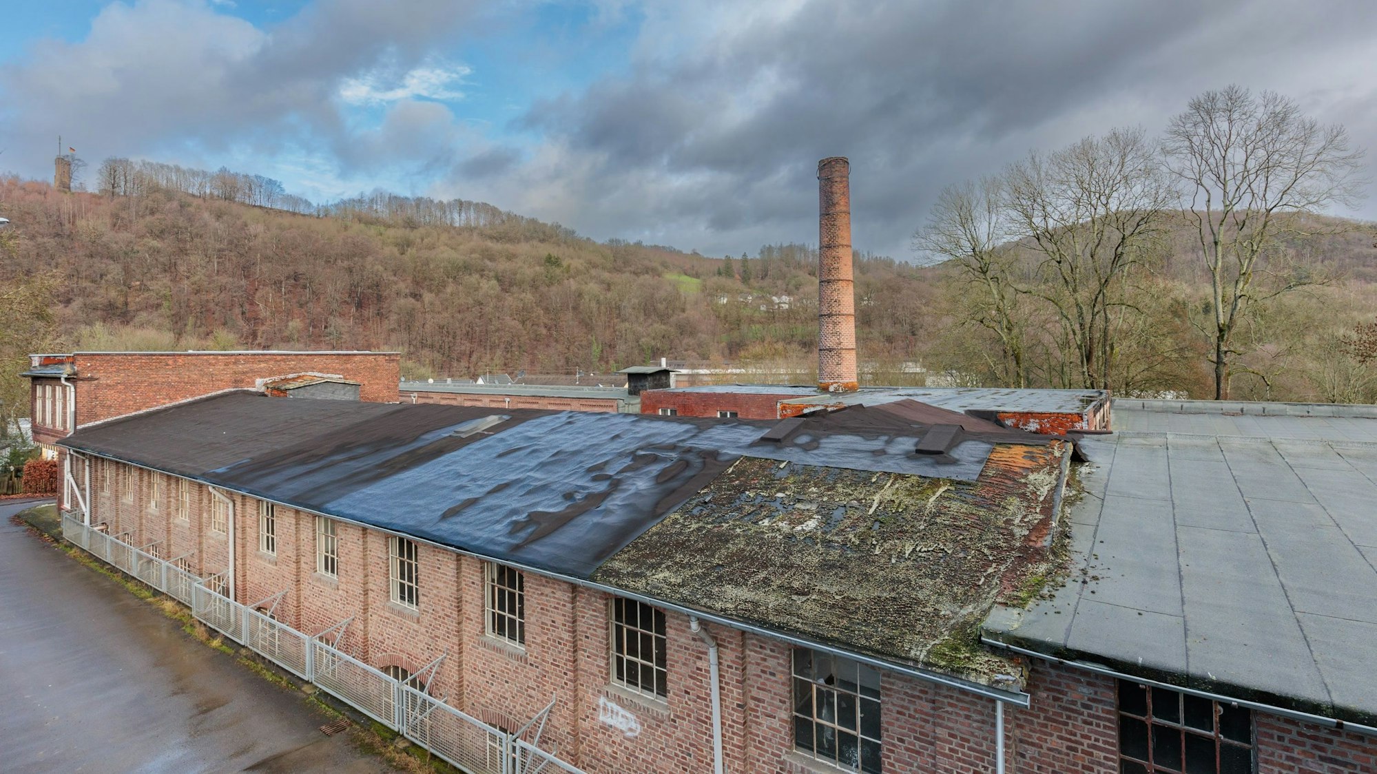 Alte Backsteinbauten mit Moos auf dem Dach, ein Schornstein im Hintergrund.