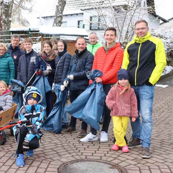 Eine Gruppe von Menschen hat sich versammelt, um Müll aufzusammeln. Sie haben blaue Müllsäcke und Zangen in der Hand.