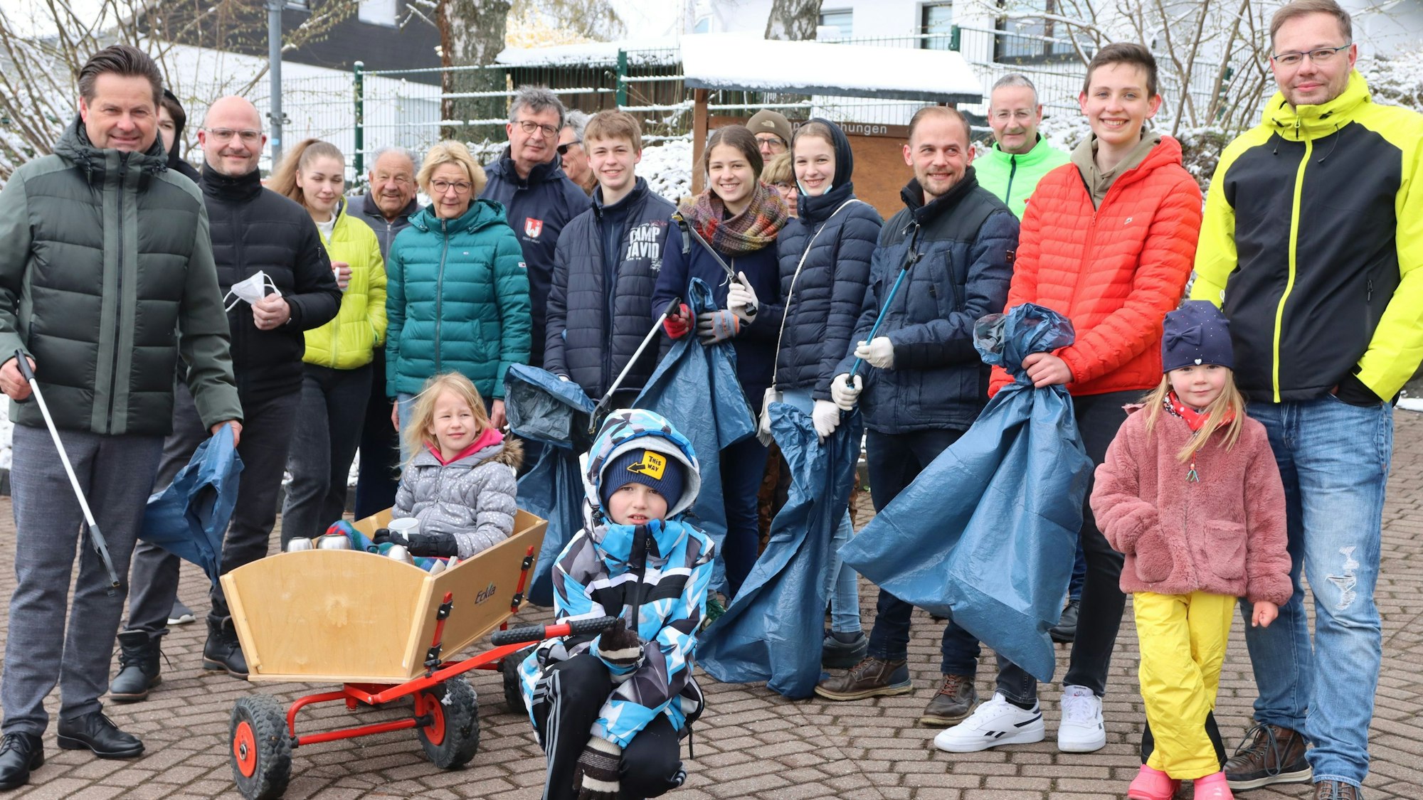 Eine Gruppe von Menschen hat sich versammelt, um Müll aufzusammeln. Sie haben blaue Müllsäcke und Zangen in der Hand.