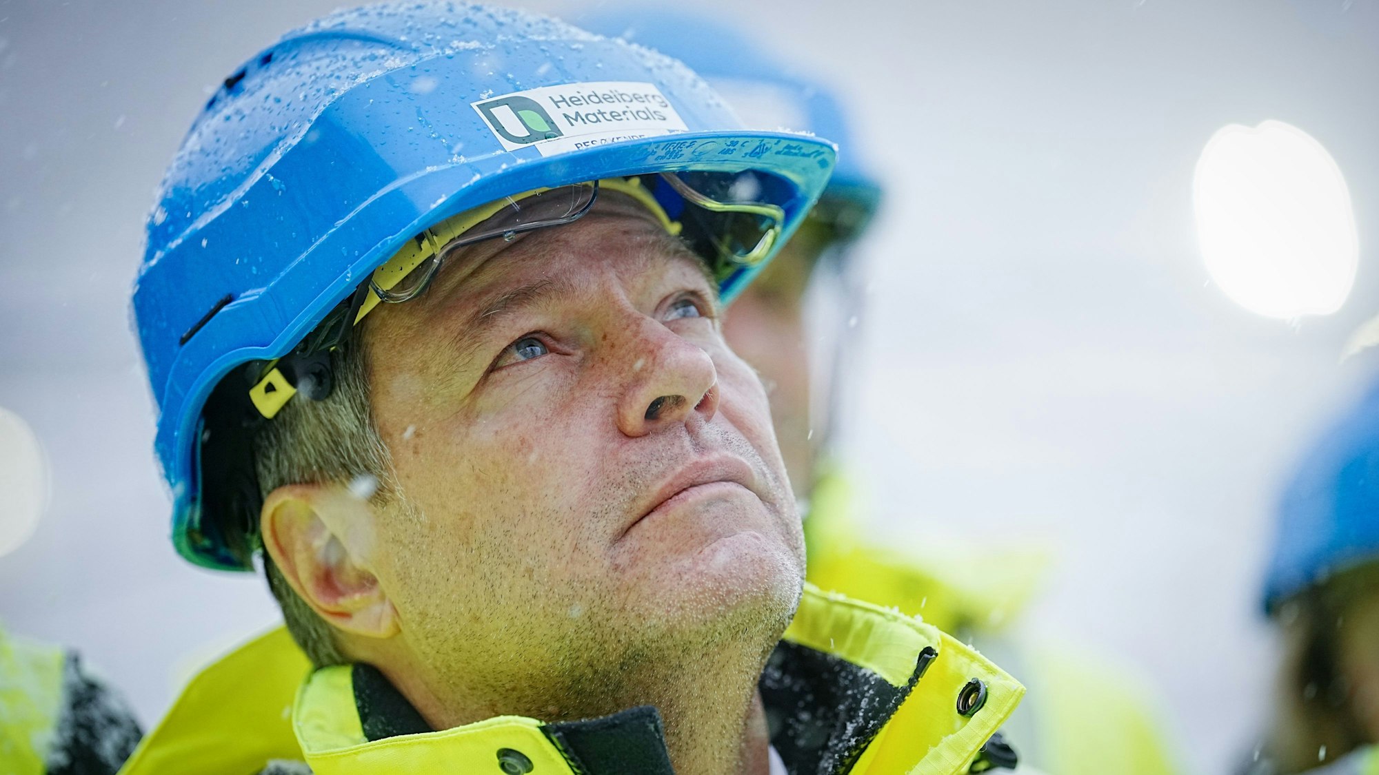 Robert Habeck mit einem blauen Helm und aufwärts gerichtetem Blick. Die Aufschrift: Heidelberg Materials.