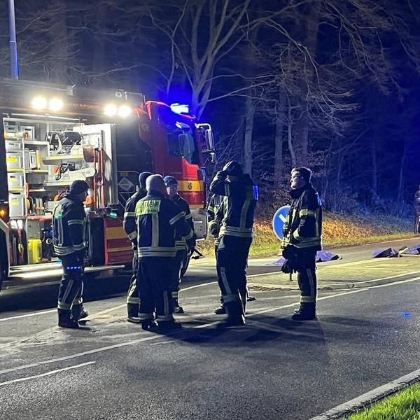 Einsatzkräfte der Feuerwehr stehen nach einem tödlichen Unfall in Hennef am Unfallort.