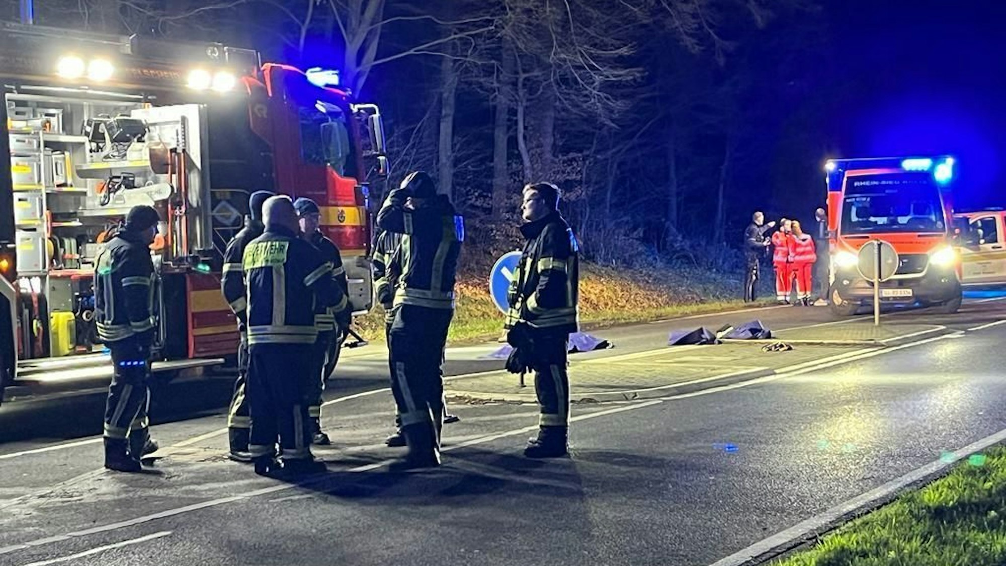 Einsatzkräfte der Feuerwehr stehen nach einem tödlichen Unfall in Hennef am Unfallort.