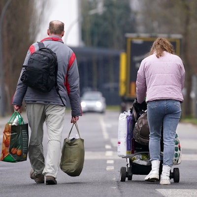 Ein aus der Ukraine geflüchteter Mann und eine Frau mit Kinderwagen verlassen mit Gepäck eine Flüchtlingsunterkunft.