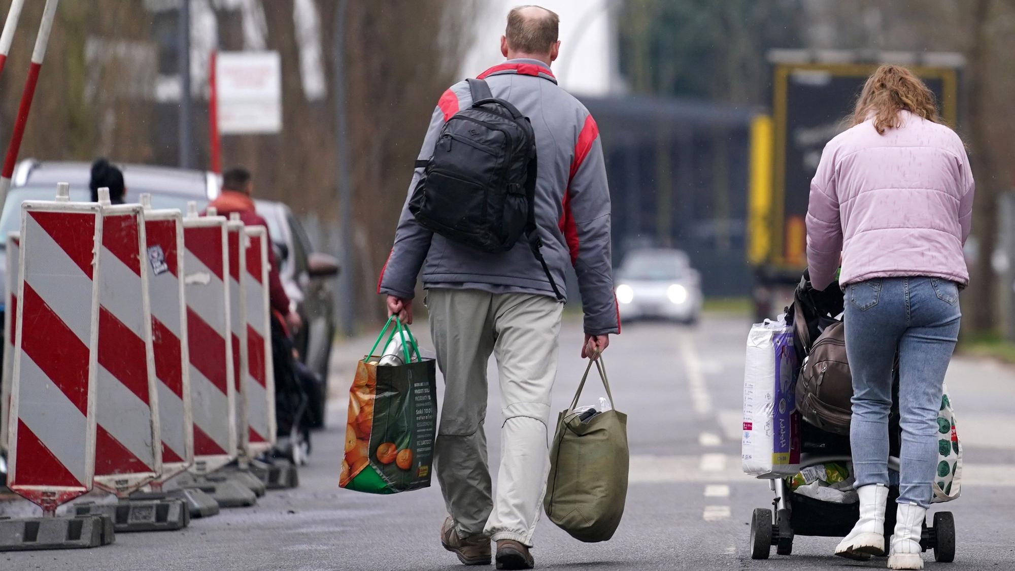 Ein aus der Ukraine geflüchteter Mann und eine Frau mit Kinderwagen verlassen mit Gepäck eine Flüchtlingsunterkunft.