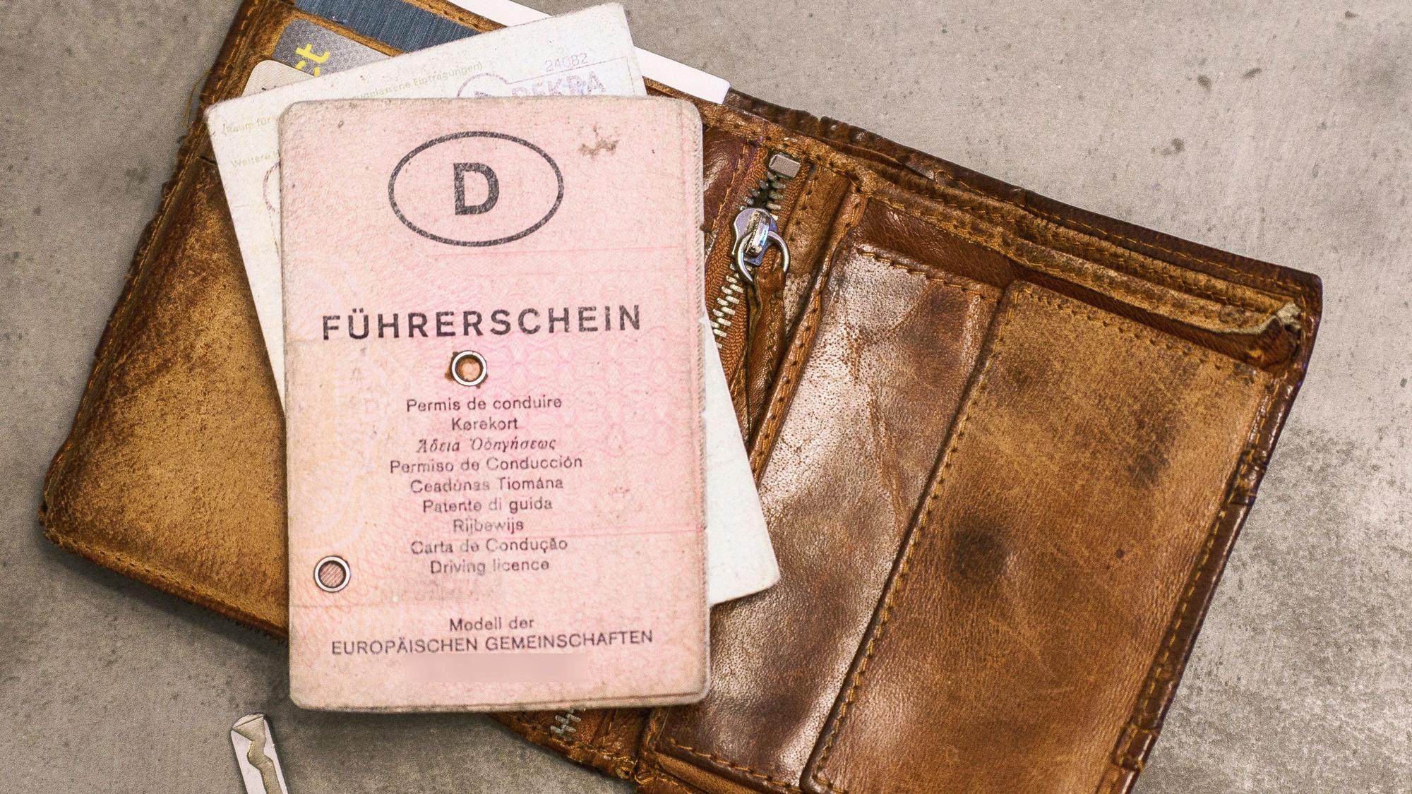 Ein rosafarbener Führerschein in Papierform liegt auf einem Geldbeutel neben einem Autoschlüssel.