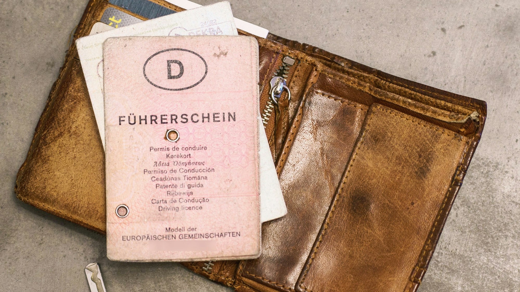 Ein rosafarbener Führerschein in Papierform liegt auf einem Geldbeutel neben einem Autoschlüssel.