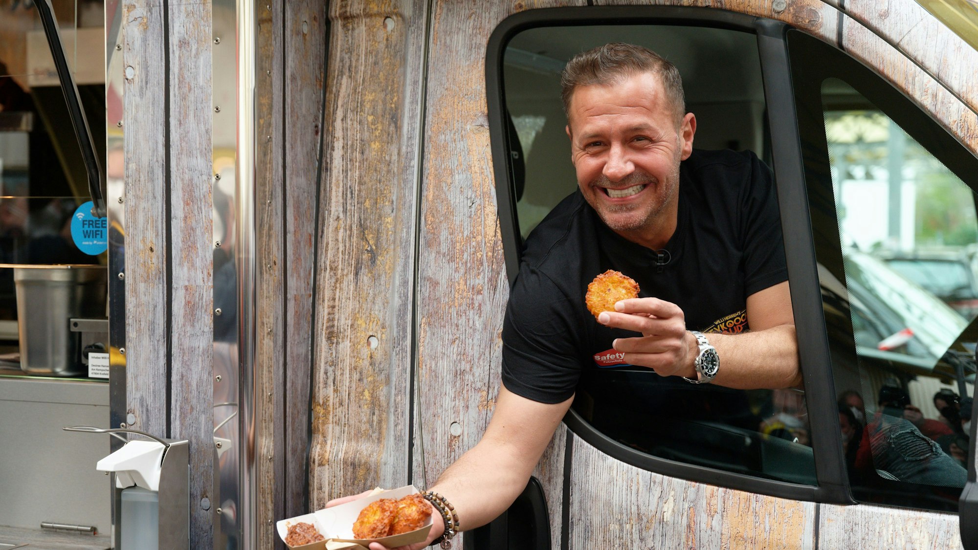 Schauspieler und Reality-Star Willi Herren isst bei der Eröffnung von „Willi Herren’s Rievkooche Bud“ einen Reibekuchen.