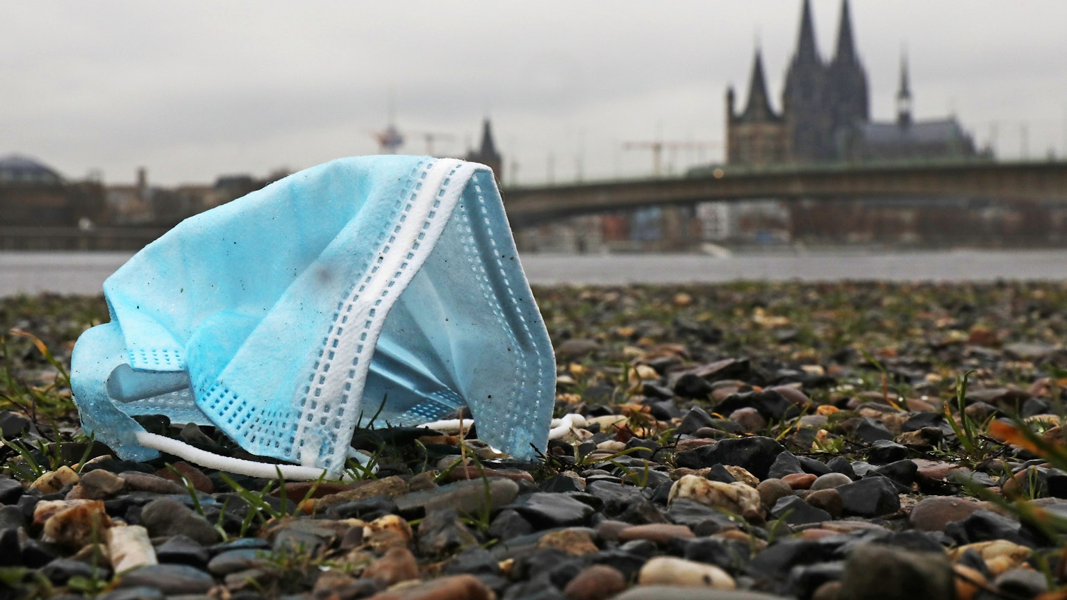 Eine weggeworfene Maske liegt am Rheinufer auf dem Boden. Im Hintergrund ist der Dom zu sehen. In Nordrhein-Westfalen galten strenge Regeln, um die Ausbreitung des Coronavirus zu verhindern.