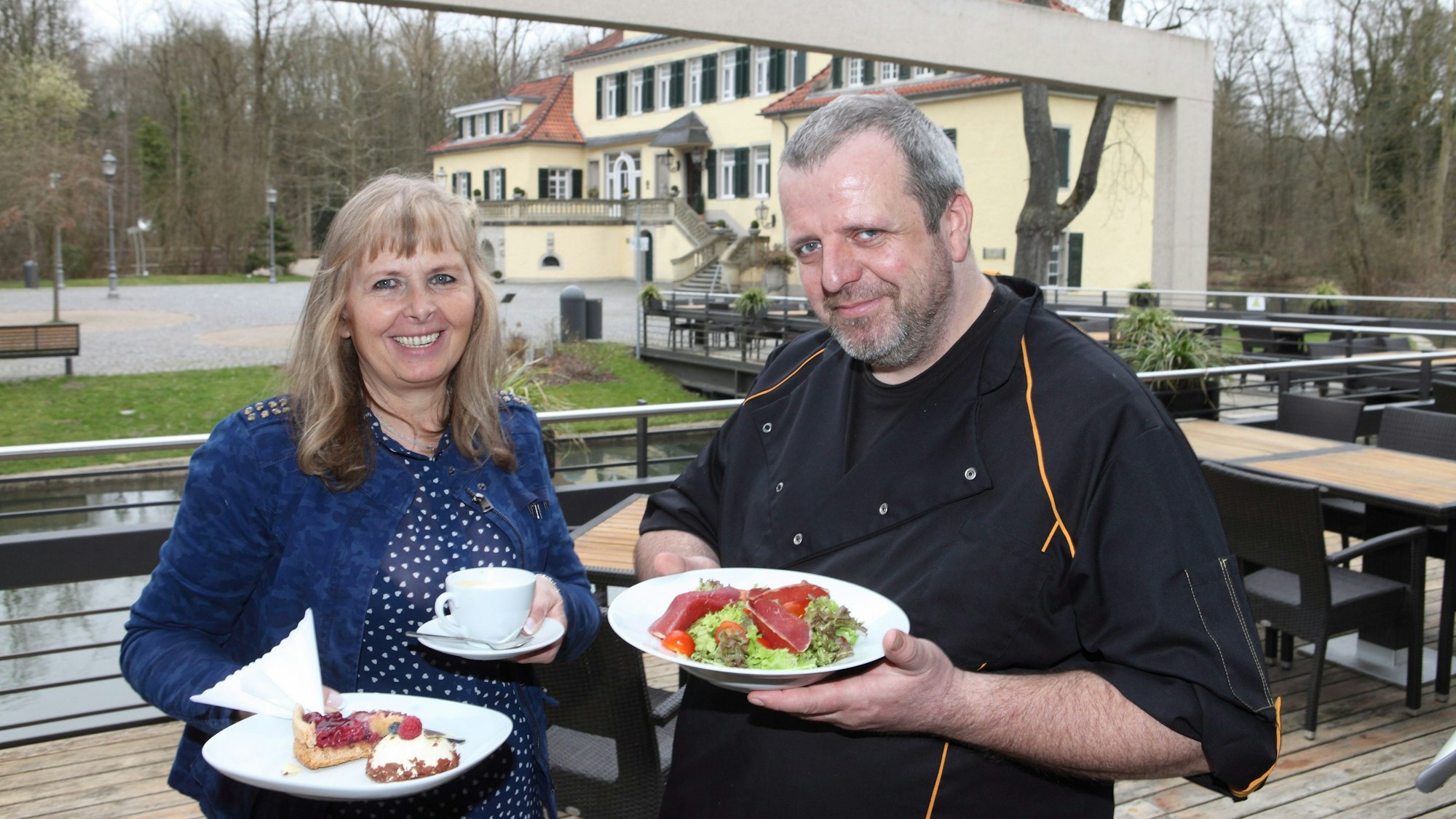 Marlene Jablonski-Reicheltsteht mit Koch Mario Arke vor dem Schloss und hält Teller mit Gerichten darauf in der Hand.