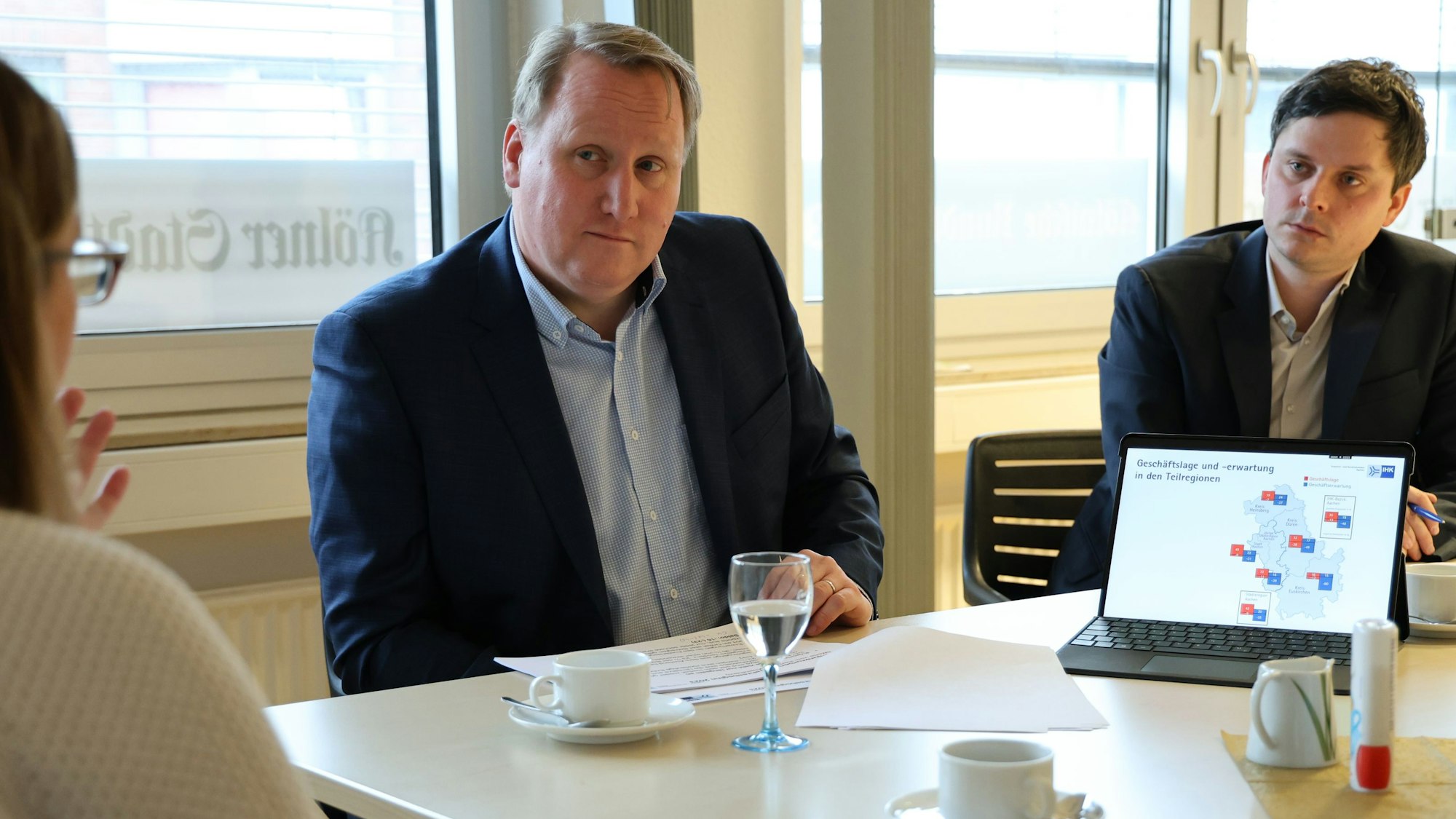Zwei Männer sitzen am Tisch und erläutern eine Grafik, die auf einem Laptop dargestellt wird.
