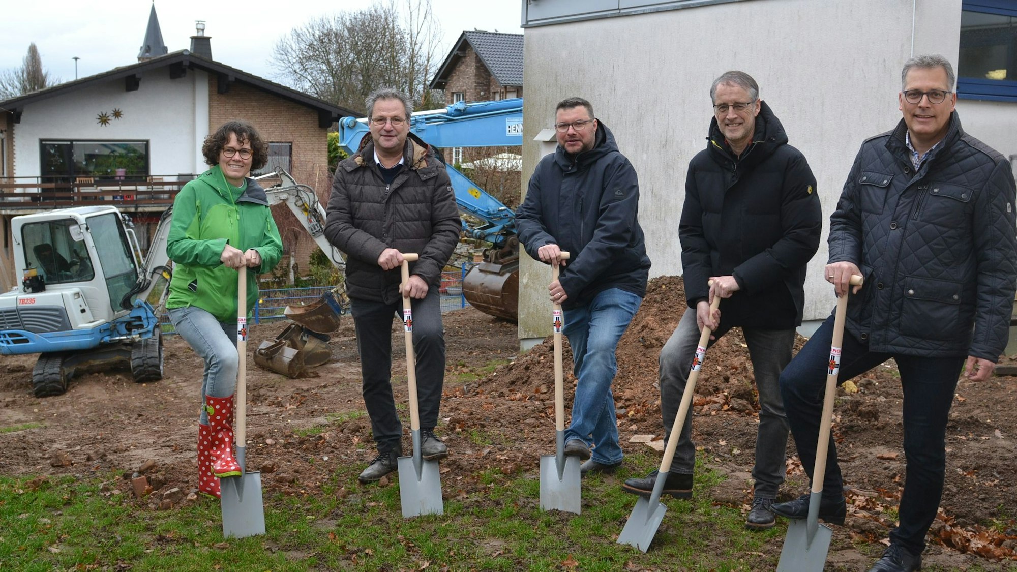 Eine Frau und vier Männer stehen mit Schaufeln im Hof