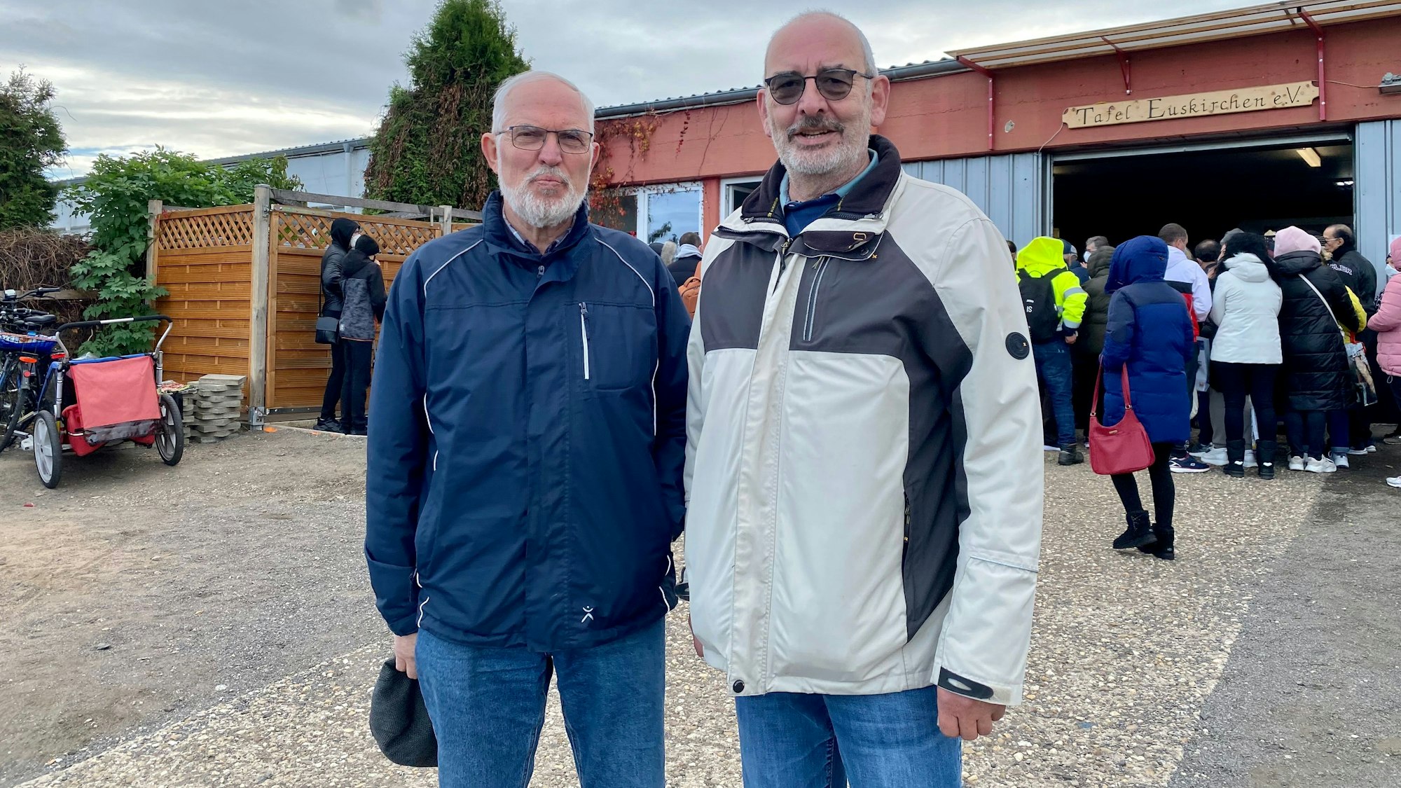 Die beiden Leiter vor der Euskirchener Tafel. Im Hintergrund warten Abholer, um ins Gebäude an der Gottfried-Daimler-Straße eingelassen zu werden.