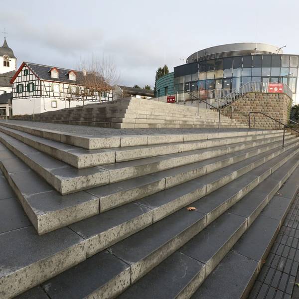Eine breite Treppenanlage führt zu einem ovalen Gebäude mit einer Glasfront.