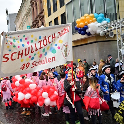 Im ersten Zug nach der Pandemie werden am Karnevalssonntag deutlich weniger Teilnehmende bei den Schull- un Veedelszöch mitgehen. Schüler halten ein Transparent mit der Beschriftung "Schullzöch 2020 - 49 Schulen".